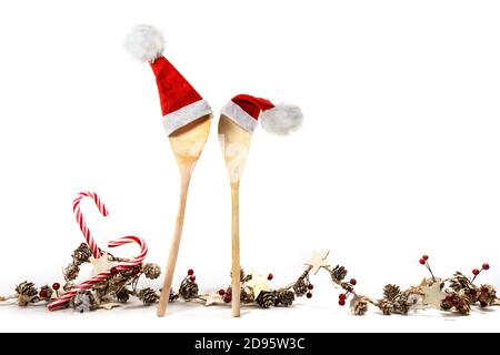 Two wooden cooking spoons with red Santa Claus hats and a Christmas decoration garland, with candy canes, cones, stars and artificial berries, isolate Stock Photo