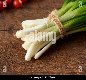 bundle of green onions tied with a rope on a brown cutting board, close up.
