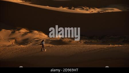 Woman traveler is walking on red sand dunes at sunset Stock Photo