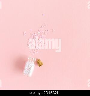 Tiny glass jar with a cork, scattered white stars sequins on a pink pastel background Stock Photo