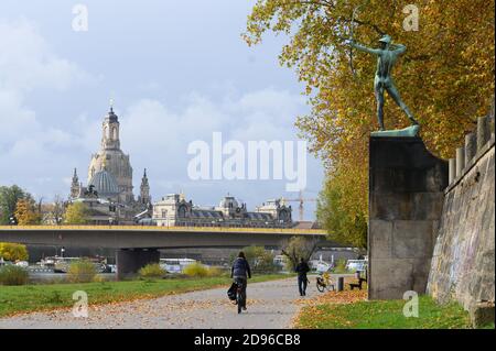 Dresden, Germany. 03rd Nov, 2020. A cyclist is riding along the banks of the Elbe passing the sculpture 'Archer' by Ernst Moritz Geyger, with the Frauenkirche in the background. Credit: Sebastian Kahnert/dpa-Zentralbild/ZB/dpa/Alamy Live News Stock Photo
