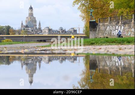 Dresden, Germany. 03rd Nov, 2020. Cyclists ride along the banks of the Elbe in front of the Frauenkirche and the sculpture 'Archer' by Ernst Moritz Geyger and are reflected in a puddle. Credit: Sebastian Kahnert/dpa-Zentralbild/ZB/dpa/Alamy Live News Stock Photo