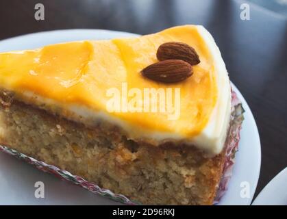 Close-up of a slice of carrot cake with orange icing and almonds on top Stock Photo