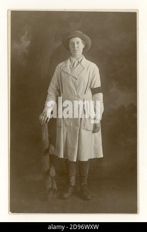 Original WW1 era studio portrait postcard of typical attractive young Land Girl wearing the standard uniform of breeches, felt hat, a knee-length overall tunic (with a button-fastening integrated belt) leather leggings and boots with national service armband denoting that she has served for 3 months  in the Women's Land Army (WLA) Liverpool, England,  U.K. circa 1917 1918