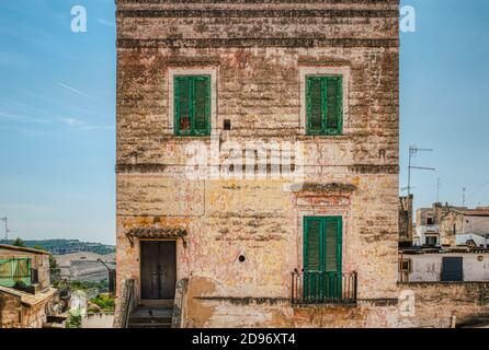 Worn byzantine house facade in southern Italy with old louvered shutters or louvres and decadent exterior. Building exterior with green jalousies Stock Photo