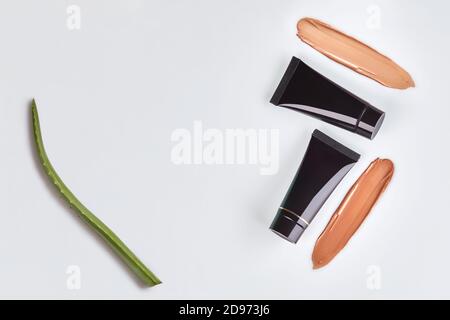 Two black tubes of tone cream, foundation smeared by surface, green leaf of aloe isolated on white. Cosmetic packaging. Close up, copy space Stock Photo