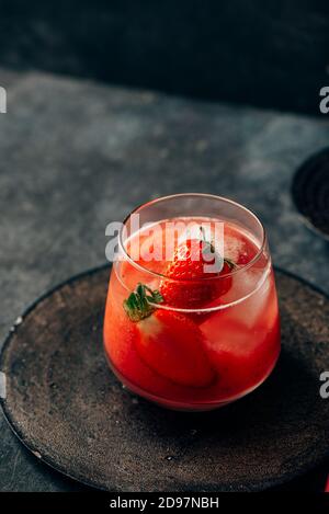 Delicious strawberry cocktail. Fresh summer cocktail with natural strawberry and ice cubes. Glass of strawberry soda drink on grunge dark background. Stock Photo