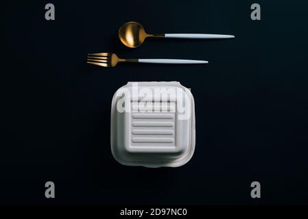 Delivery Healthy food concept: white burguer packaging closed with golden fork and spoon in cardboard lunch box to take to the office on black backgor Stock Photo