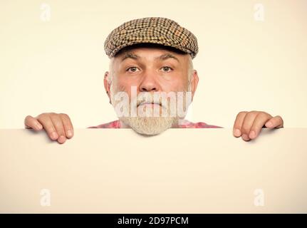 Senior bearded emotional man peek out of banner place announcement. Pensioner grandfather in vintage hat poster information copy space. Elderly person. Announcement concept. Event announcement. Stock Photo