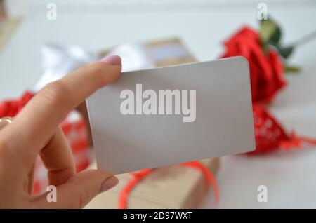 Girl holds a blank card without an inscription on the background of gifts with bows, ribbons and red rose on a white background. concept of discounts, Stock Photo