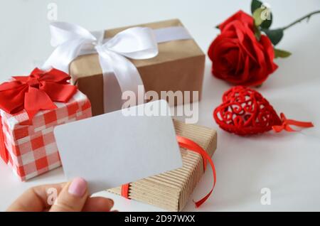 Girl holds a blank card without an inscription on the background of gifts with bows, ribbons and red rose on a white background. concept of discounts, Stock Photo