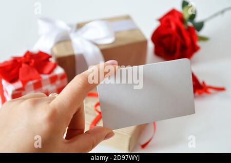 Girl holds a blank card without an inscription on the background of gifts with bows, ribbons and red rose on a white background. concept of discounts, Stock Photo