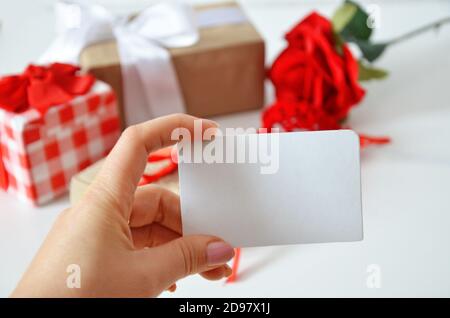 Girl holds a blank card without an inscription on the background of gifts with bows, ribbons and red rose on a white background. concept of discounts, Stock Photo