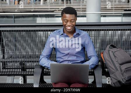 Portrait of african american young man sitting on bench with bags and laptop Stock Photo