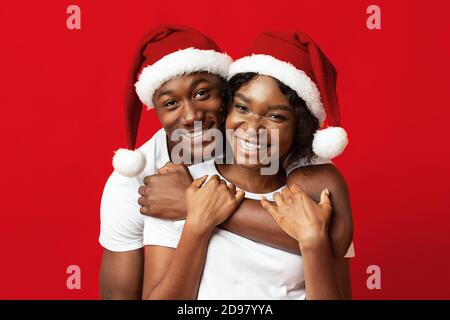 Young black lovers in Santa hats having fun on red Stock Photo