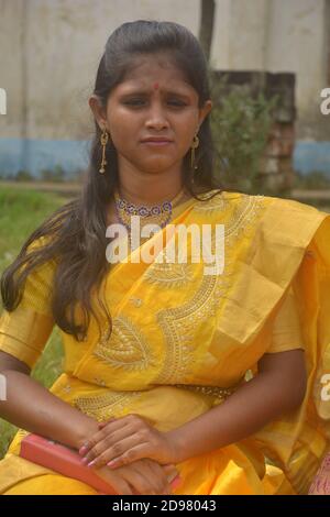 Close up of a teenage Indian girls wearing sari and golden nose ring maang tikka necklace earrings bangles with make up sitting on a field. Stock Photo