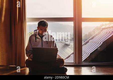 Man using laptop sitting near big window in wooden cottage Stock Photo