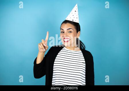 Young beautiful woman wearing a birthday hat over insolated blue background smiling and thinking. Remembering something Stock Photo