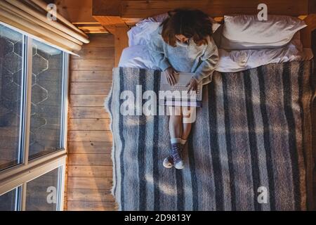 Woman working on laptop sitting on cozy bed Stock Photo