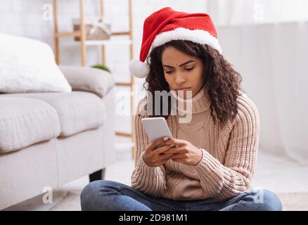 Black lady in santa hat using cellphone, looking sad Stock Photo
