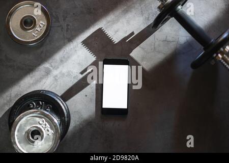 Mobile phone with white screen on a surface with dumbbells and different iron weight plates Stock Photo