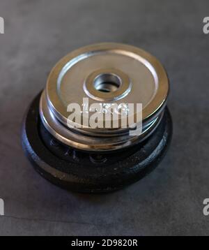 Iron weight plates of different sizes and weights stacked on a concrete surface Stock Photo