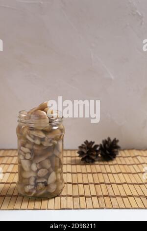 Pickled forest mushrooms in a glass jar with pine cones on a wooden background. Autumn gifts. Vertical orientation. Copy space. Stock Photo