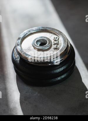Iron weight plates of different sizes and weights stacked on a concrete surface Stock Photo