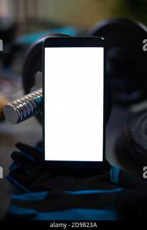 Mobile phone surrounded by different elements for sports training such as dumbbells, plates for weights, grip for push-ups, a rope to jump ... Stock Photo