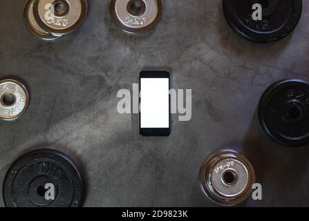 Mobile phone on a concrete surface with weight plates of different weights, sizes and colors with empty space Stock Photo