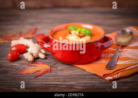 Homemade tomato soup with ginger, shrimps and basil on a brown wooden background, copy space Stock Photo