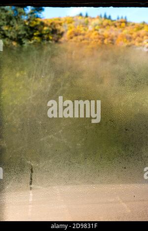 looking through a window, partly obscured by water condensation on the glass, onto a forested hill covered with trees in autumn Stock Photo