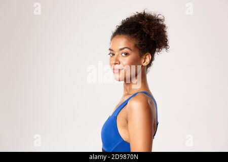 Concept of workout and sport. Close-up of young athletic woman in fitness clothing, turn head at camera with confident smile, white background Stock Photo