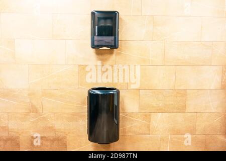 Paper towel black dispenser and a trash can at the bottom for used paper towels on the wall in a public toilet Stock Photo