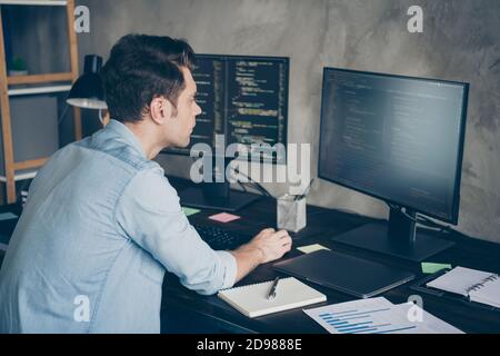 Back rear spine view photo of focused guy it specialist sit desktop work computer testing new operating system wear denim jeans shirt in modern Stock Photo