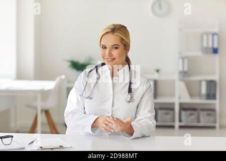 Woman therapist in white uniform sitting in office and looking at camera during videocall with patient Stock Photo