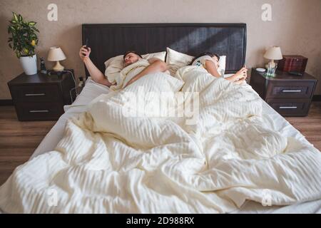 couple laying in bed surfing internet on phone Stock Photo