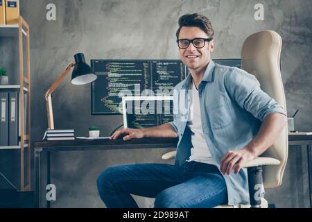 Portrait of positive guy it specialist sit chair desk enjoy working pc home ready debugging java script cyber space error wear denim jeans shirt in Stock Photo
