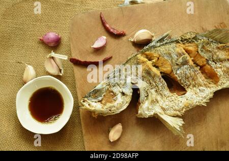 deep fried salty bass fish with soy sauce on wooden chop block Stock Photo