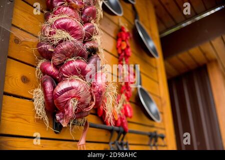 A bundle of Mediterranean vegetables onions, chillies hanging to dry in a market stall.Dried Mixed herbs Chillies, Onions and garlics hang on wooden Stock Photo