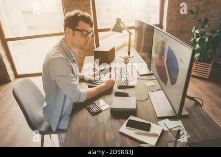 Profile side photo of focused guy sit desk look monitor computer screen see charts funds statistics data work with hardware in modern home office Stock Photo