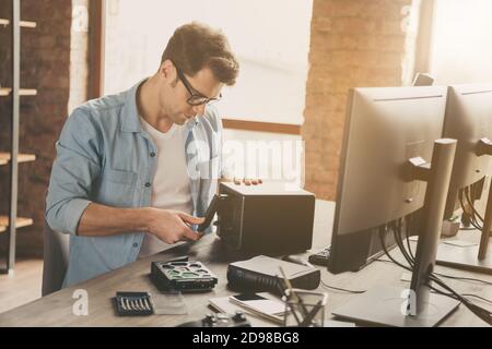 Photo of focused guy software support master sit desk repair hard drive disk operating system wear denim jeans shirt in workstation Stock Photo