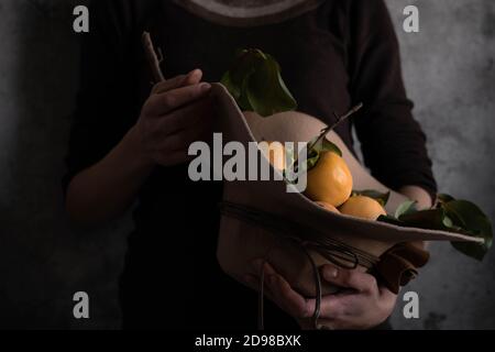 Close up view of woman holding an autumn hat with raw persimmons. Still life,  fine art concept Stock Photo