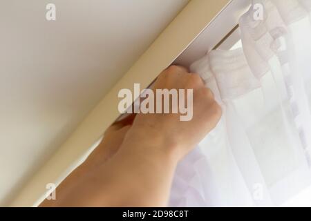 Hands of a young man hang curtains on the ledge on the window Stock Photo