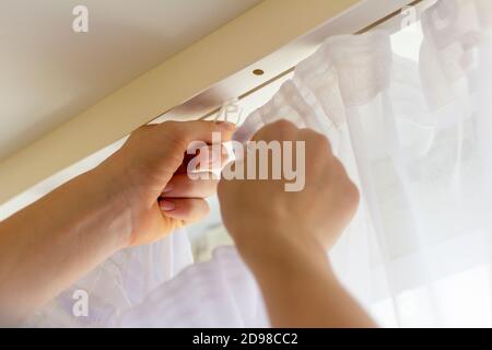 Hands of a young man hang curtains on the ledge on the window Stock Photo