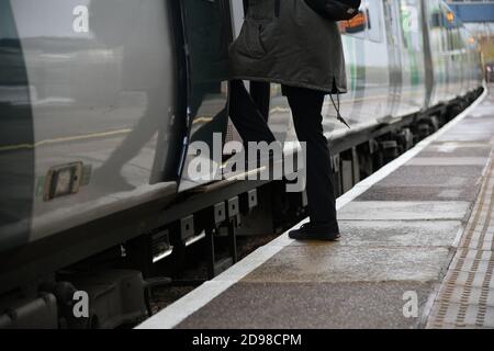 Person boarding a train in the United Kingdom showing the Platform Train Interface with a high stepping distance on a curved platform Stock Photo