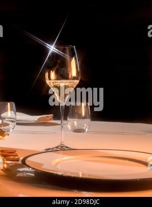 glass of champagne on table setting at restaurant, star light reflections on black background Stock Photo
