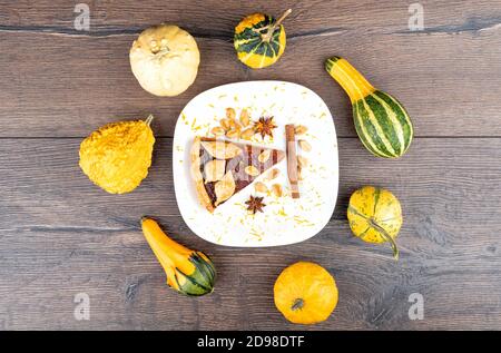Top view of a slice of pumpkin tart in a plate with cinnamon, star anise and orange zest. Plate with a piece of pumpkin tart and mini pumpkin around. Stock Photo