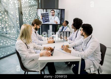 Medical and healthcare concept. Team of multiethnic diverse doctors scientists, watching online webinar with young experienced Caucasian doctor Stock Photo
