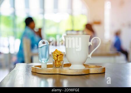 Mini portable alcohol gel bottle to kill Corona Virus(Covid-19) and biscuits and coffee cup on table with blurred image of a family eating at restaura Stock Photo